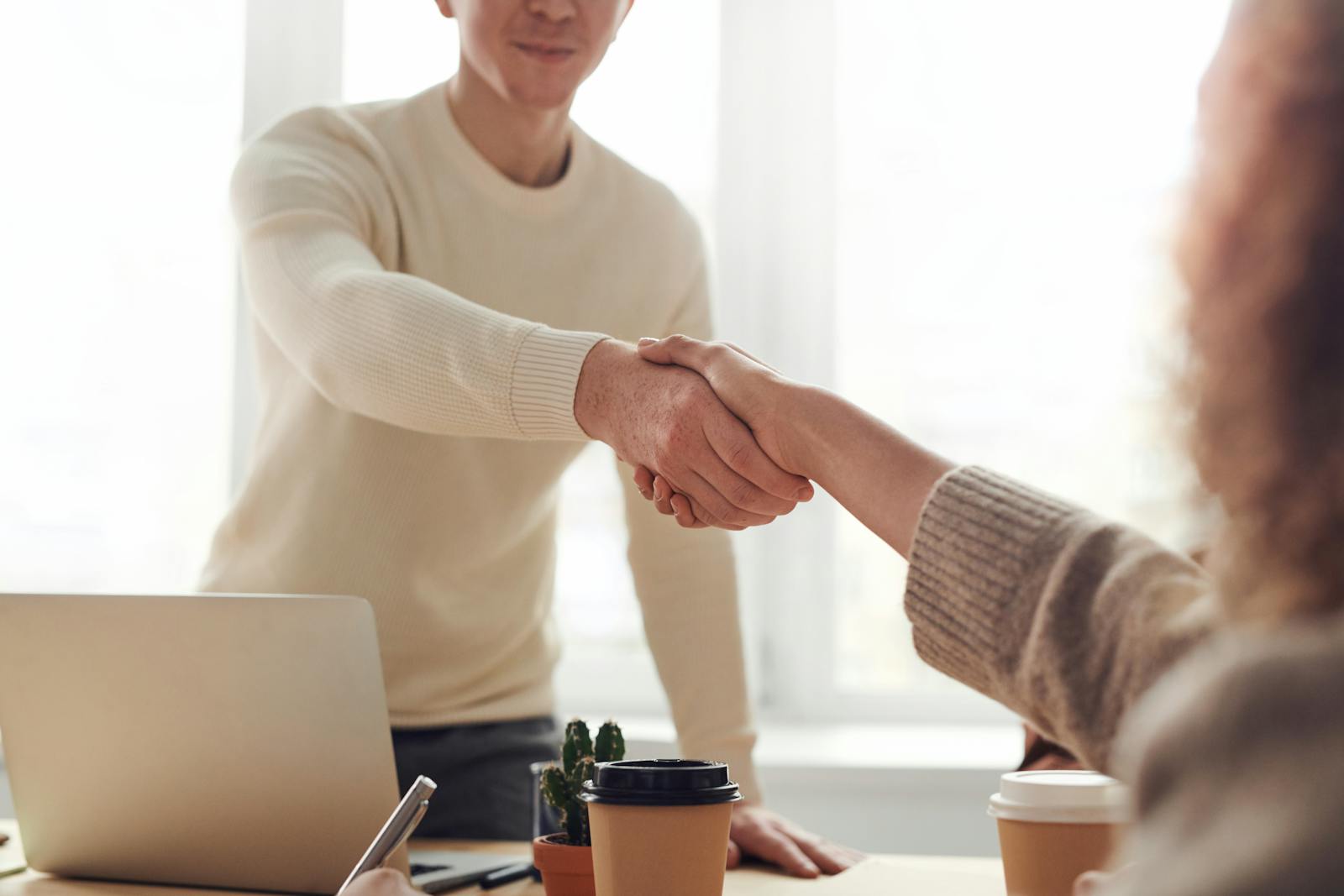 Two people meeting over a laptop and coffee at a wooden desk.